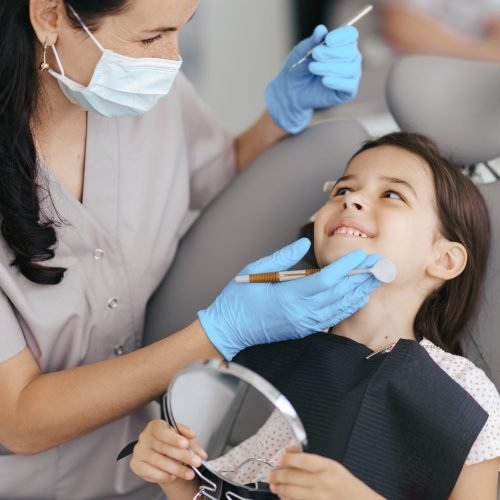 Cute little girl sitting on a modern dental chair and having dental consultation with dentist