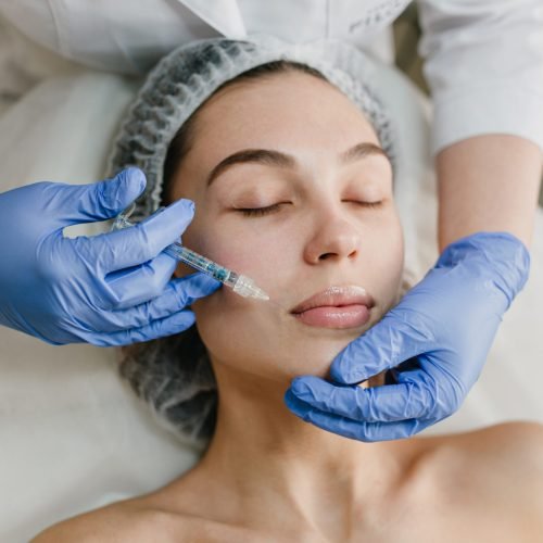 Portrait young woman during cosmetology procedures in beauty salon. Injecting, botox,  hands in blue glows, healthcare, therapy, lips, beauty